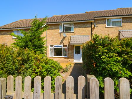 A front yard with bushes and a wooden fence leading to the entrance of a two-story brick house at Howards Hill West in Cromer