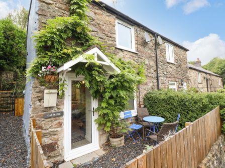 The exterior of a stone cottage with a small patio area with a blue table and chairs and plants at Cartrefle in Rhyd Uchaf near Bala