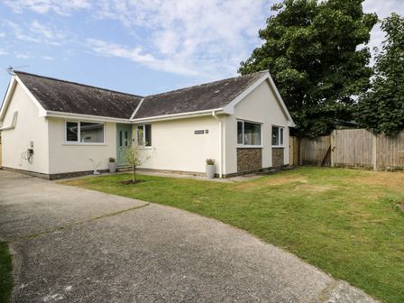 A single-story house with a green door surrounded by grass and a concrete driveway at GaGa Ar y Traeth in Morfa Bychan