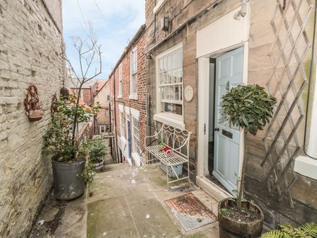 A small outdoor stone patio with potted plants and a white metal bench next to a door at Sailing By in Whitby