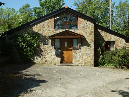 The front view of a stone barn with a wooden door and windows surrounded by trees at Dilly Dally Barn Bradworthy near Bude