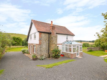 A stone and white two story house with a glass conservatory and gravel driveway in a rural setting at The Old Farmhouse Upper Pitts in Knighton
