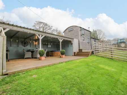 An outdoor covered patio with chairs a table and a hot tub next to a wooden cabin on a lawn at Shepherds Cabin at Titterstone in Clee Hill