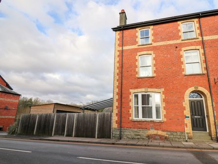 A red brick building with multiple windows and a black door next to a wooden fence and a wooden shed at Afonwy House in Rhayader