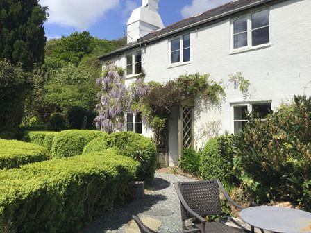 The exterior of a white two-story house with a garden path hedge and outdoor table and chairs at Crannacombe Farmhouse in Loddiswell