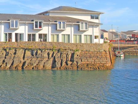 A waterfront building with multiple windows and a stone retaining wall by the water at Glaslyn Retreat in Porthmadog