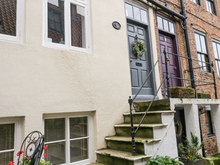 An outdoor view of stairs leading to two doors on a white and brick building with windows and plants nearby at Robins Nest in Whitby