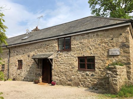 A stone house with brown windows and door with flowers outside at Chilvery Farm Cottage Throwleigh near Chagford