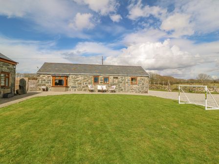 A stone cottage with wooden framed windows and outdoor seating on a lawn with a small soccer goal at Beudy in Chwilog