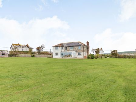 A large house with solar panels on the roof and a glass extension surrounded by a grassy field at Penhallick House in Tintagel