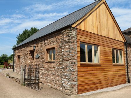 An exterior view of a stone and wood cottage with windows and a small gate at The Cottage in Treborough near Washford