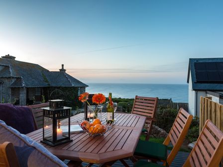 An outdoor wooden table with chairs candles flowers and fruit bowl overlooking the sea at Godrevy in St Ives