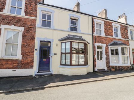 A row of brick and painted terraced houses with bay windows and front doors on a street at Chwech in Menai Bridge