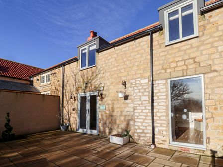 An outdoor patio area with stone walls and glass doors at The Pheasantry in Irton Moor near Scarborough