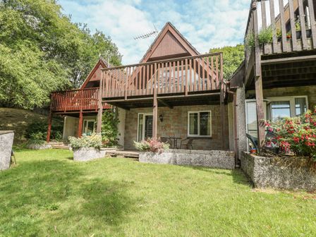 A backyard with grass and plants in front of a house with wooden balconies and patio furniture at Running Waters in Callington
