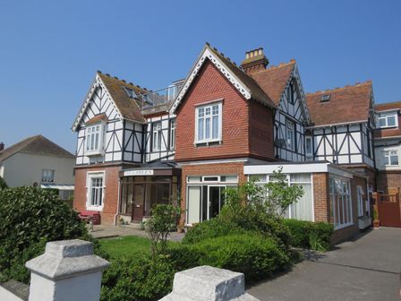 A large house with white and black timber framing and red brick sections surrounded by shrubs in Swanage