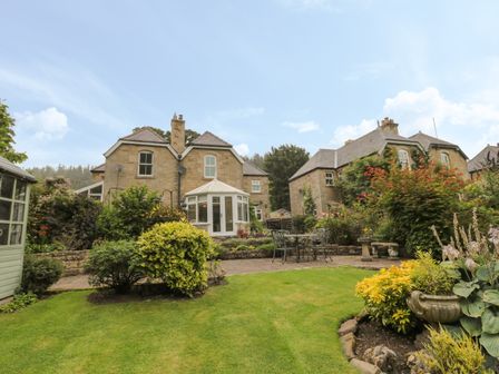 A garden with lawn bushes and outdoor furniture behind stone houses at Red Squirrel Cottage 5 Biddlestone in Rothbury