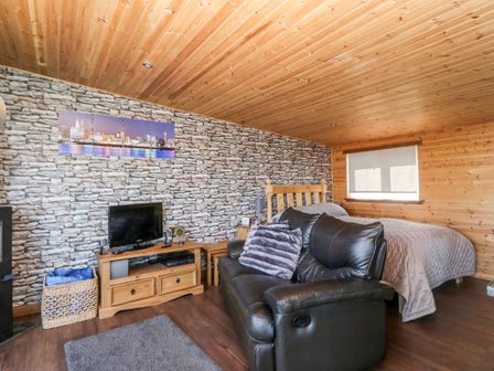 A bedroom with a wooden bed a black leather sofa a TV on a wooden stand and a stone wall at Blackbrae Cabin in Glenboig near Coatbridge Glasgow and Stirling