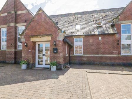 The front entrance of a brick building with double glass doors two lantern lights and two flower pots on a paved area at Carpenters Cottage in Cockermouth
