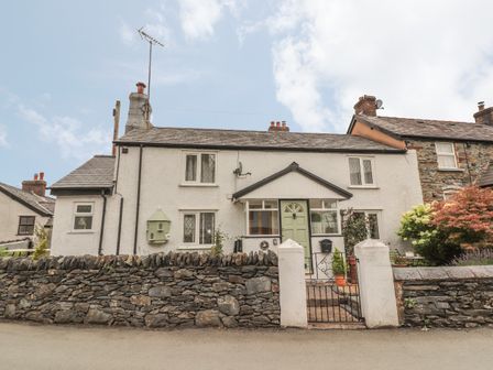 A cottage with a green door behind a stone wall and metal gate at Dove Cottage in Llanfair Talhaiarn