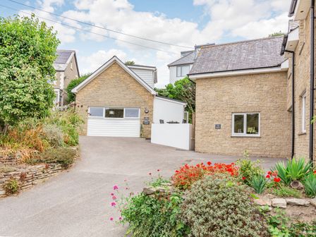 A driveway leading to garages and stone houses with plants and flowers in the foreground at The Beach House in Crantock