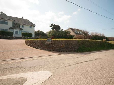 A driveway with a stone retaining wall and two houses in the background at Bay View House in Crantock