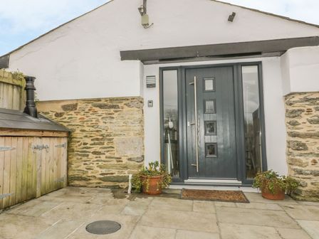 A stone paved entrance with a dark gray door flanked by glass panels and two potted plants at The Bolthole in Crantock