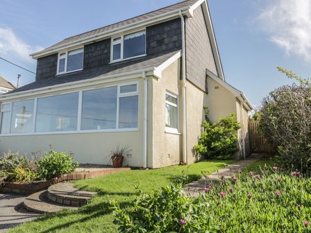 Exterior view of a two-story house with brick steps and a garden with flowers at Crantock Bay House in Crantock