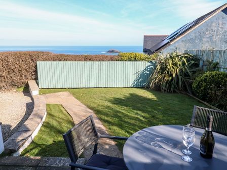 A garden with a round table and two chairs and a view of the sea at Kittiwake in Crantock