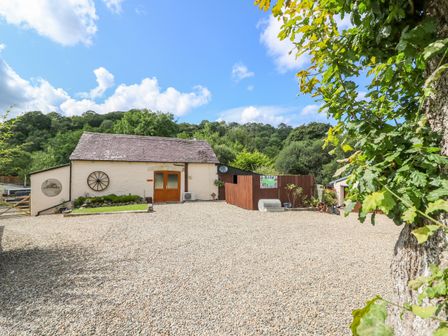 A cottage with wooden doors surrounded by gravel and trees at The Mill in Penrhiwllan