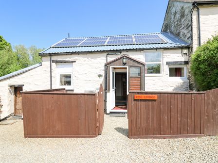 Exterior view of a stone cottage with solar panels on the roof a wooden fenced courtyard and an open porch at Rose Cottage in Penrhiwllan