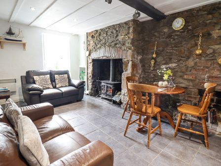 A living room with two leather sofas a wooden table with chairs and a stone fireplace at Gwenallt in Malltraeth