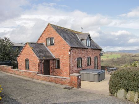 A brick house with a tiled roof and patio area with hot tub and outdoor furniture at Waggoners Cottage in Garthmyl
