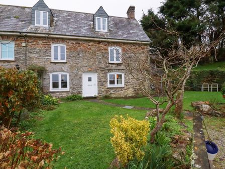 A stone house with a white door and windows a garden with grass shrubs and a leafless tree Lanvean Farmhouse Lanvean near St Mawgan