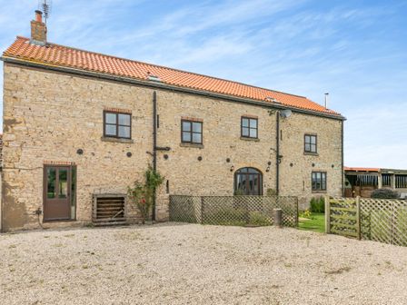 A stone building with tiled roof and multiple windows and doors surrounded by gravel and wooden fences at Stubbs Grange Barn in Askern