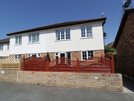 A semi detached house with white walls and red wooden fencing in front at West Shore Cottage in Llandudno