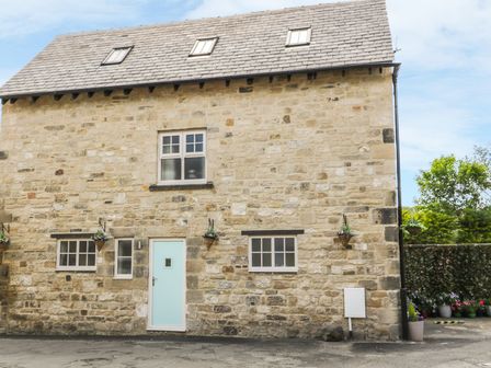 Stone exterior wall of a house with a light blue door three windows and flower baskets at River Cottage in Morpeth