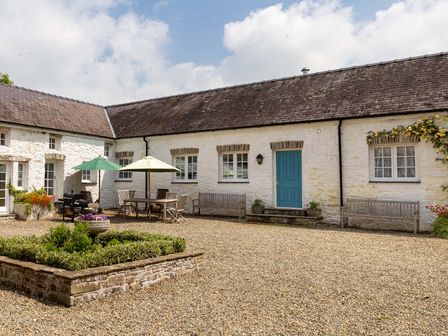 An outdoor courtyard with gravel ground stone planter wooden benches tables with umbrellas and a blue door on a stone building at The Old Carriage Court in Kidwelly