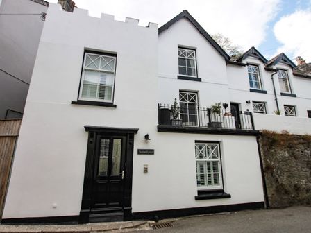 A white building with black door and windows with balcony and plants at The Shell Seekers in Fowey