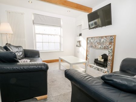 A living room with two black leather sofas a white coffee table a decorative fireplace and a wall mounted TV at 11A Church Street in Whitby