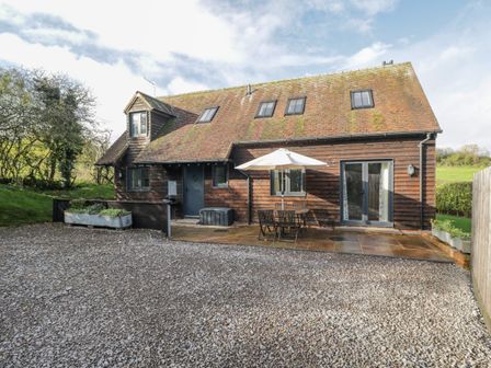 A wooden house with a gravel driveway a patio table with an umbrella and chairs at Nine Acres Barn Manton near Marlborough Wiltshire