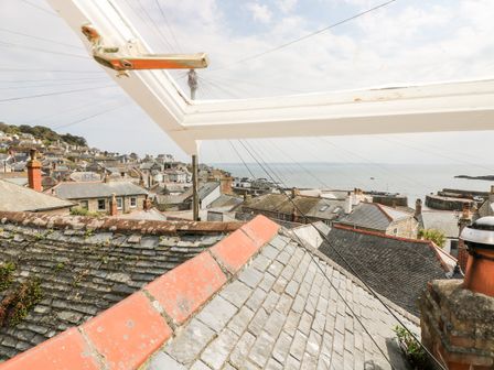 View of rooftops and chimneys with a sea horizon seen through an open window at Mole Cottage in Mousehole