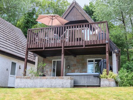 A two story house with wooden balcony and patio area with hot tub and outdoor furniture at Valley Lodge 48 in Callington