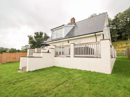A two-story house with a fenced raised patio and steps leading down to a grassy yard at Lower Pentre in Llandrindod Wells
