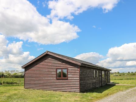 A single wooden cabin with several windows on a grassy field under a blue sky with clouds at Rose Lodge in Sheriff Hutton