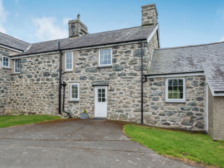 A stone house with white framed windows and a white door with a paved driveway and grass at Gwrtheyrn in Dyffryn Ardudwy