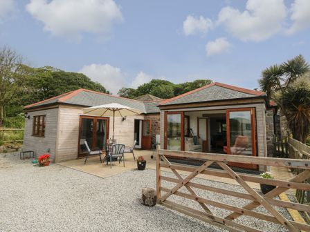 A single-story house with wooden and stone exterior a patio with table umbrella and chairs and a wooden gate at Edwin's View in Nancegollan nr Porthleven