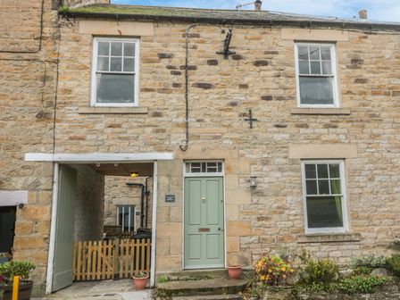 A stone house with three windows a green door and an entrance gate with potted plants at Hare & Hounds House in Allendale