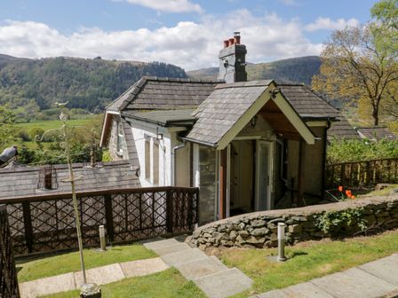 Exterior view of a small house with a stone wall and garden in a rural setting with hills in the background at The Nook in Maenan