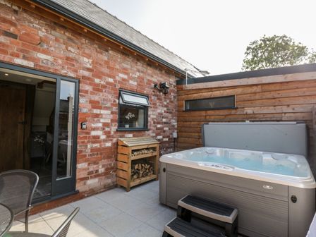 An outdoor patio with a hot tub wood storage and a sliding glass door at The Piggery in Cross Keys near Hereford